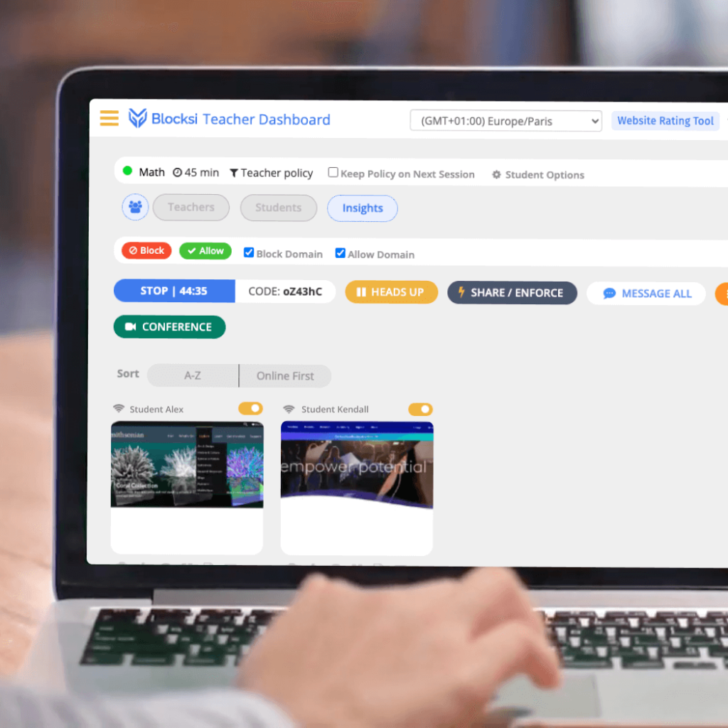An over-the-shoulder view of a person using a laptop displaying the Blocksi Teacher Dashboard, which features controls for classroom management such as student monitoring, website filtering, and policy enforcement. The dashboard shows a timer, options for blocking or allowing websites, and thumbnail previews of student activities.
